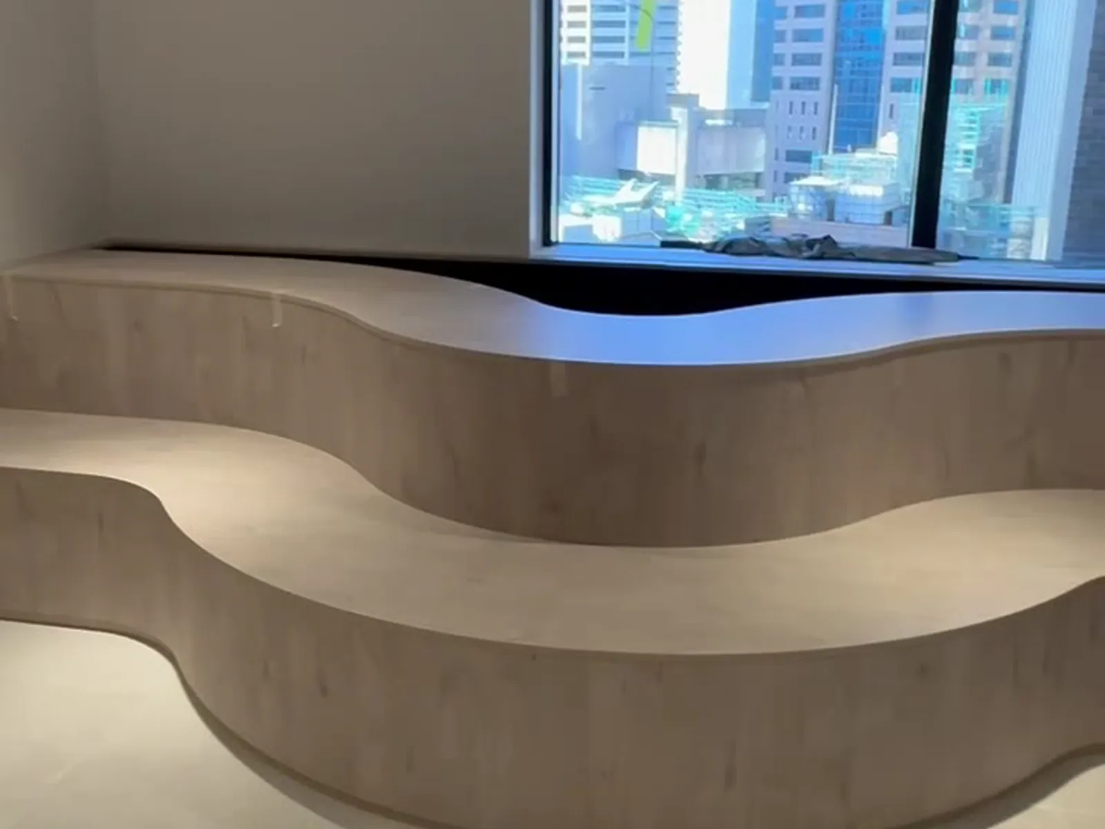 Curved timber-veneer feature bench beneath a window with a Sydney CBD skyline outlook, by FRANCA FITOUTS
